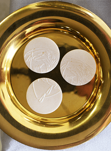 Three consecration hosts on a golden paten prepared for Catholic Mass