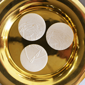 Three communion wafers on a golden plate.