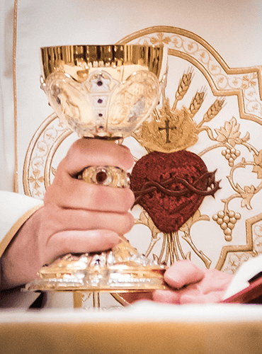 Priest holding golden chalice during Catholic Mass with Sacred Heart symbol